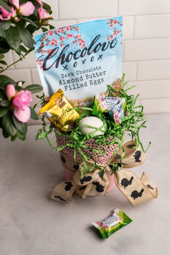 A pastel-themed Easter scene featuring a Chocolove Dark Chocolate Almond Butter Egg in its festive floral packaging. Delicate flowers and Easter decorations surround the chocolate, evoking a bright and cheerful springtime ambiance.