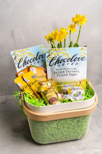 A pastel-themed Easter scene featuring a Chocolove Dark Chocolate Salted Caramel Egg in its festive floral packaging. Delicate flowers and Easter decorations surround the chocolate, evoking a bright and cheerful springtime ambiance.