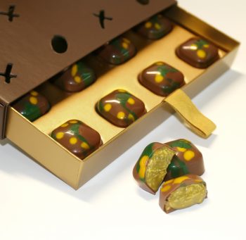 Angled view of Chocolove Dubai Style Pistachio & Kadayif Milk Chocolate Gift Box with one chocolate cut open to reveal creamy pistachio filling