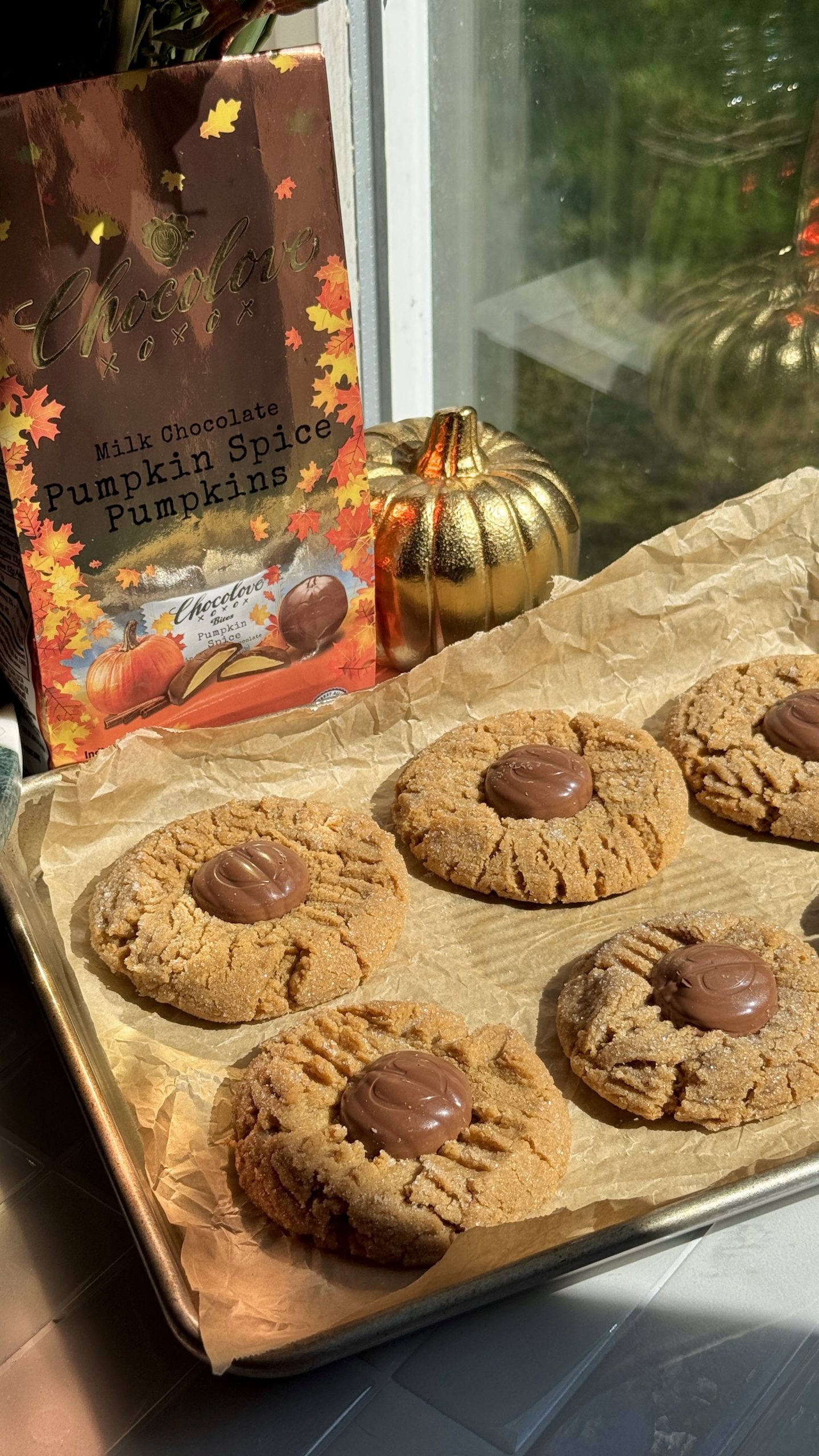 Freshly baked peanut butter cookies topped with Chocolove Milk Chocolate Pumpkin Spice Pumpkins on a parchment-lined baking sheet beside fall décor and Chocolove packaging.